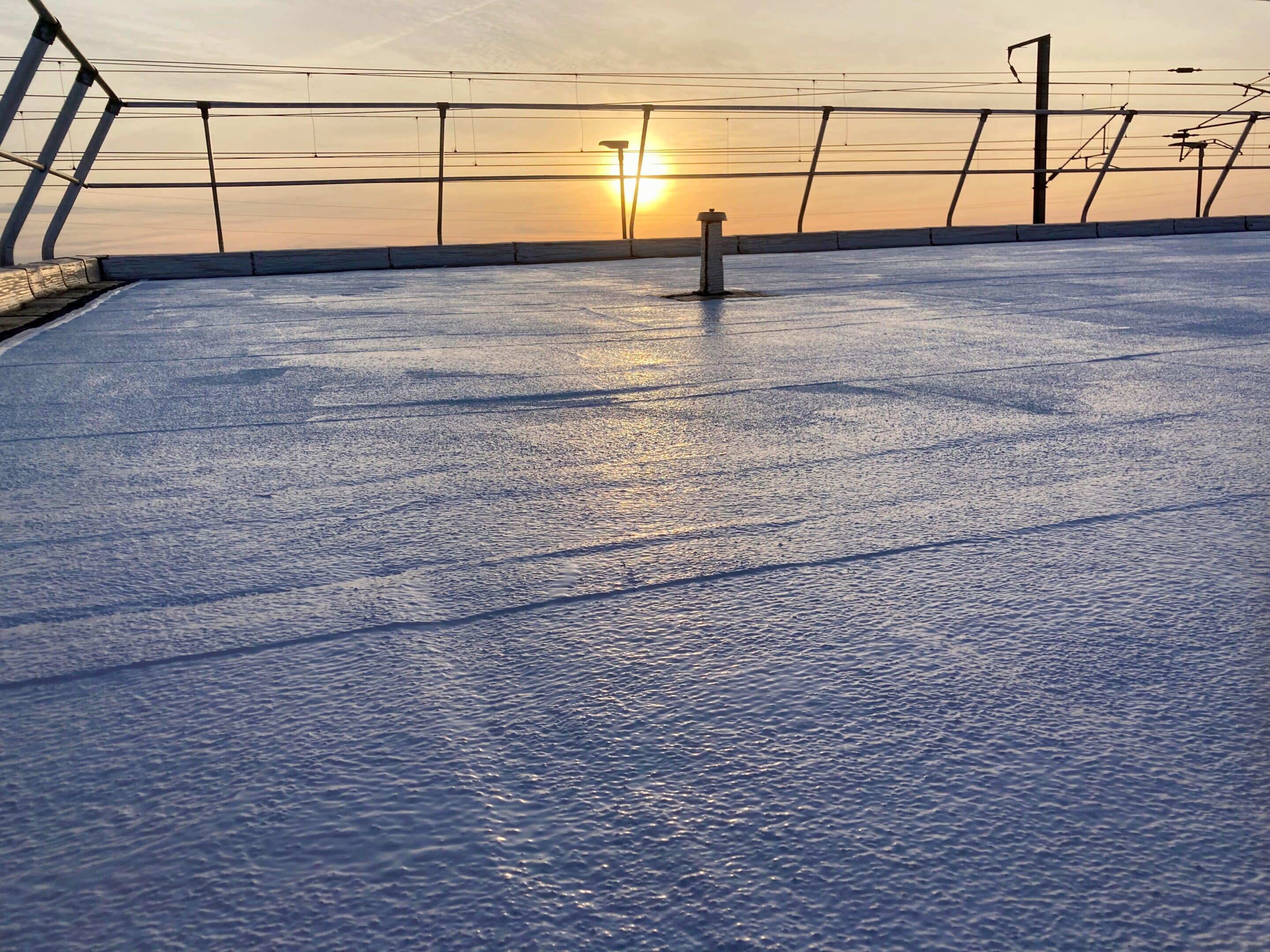 Surface d'un toit plat avec une finition blanche, éclairée par le coucher de soleil en arrière-plan.
