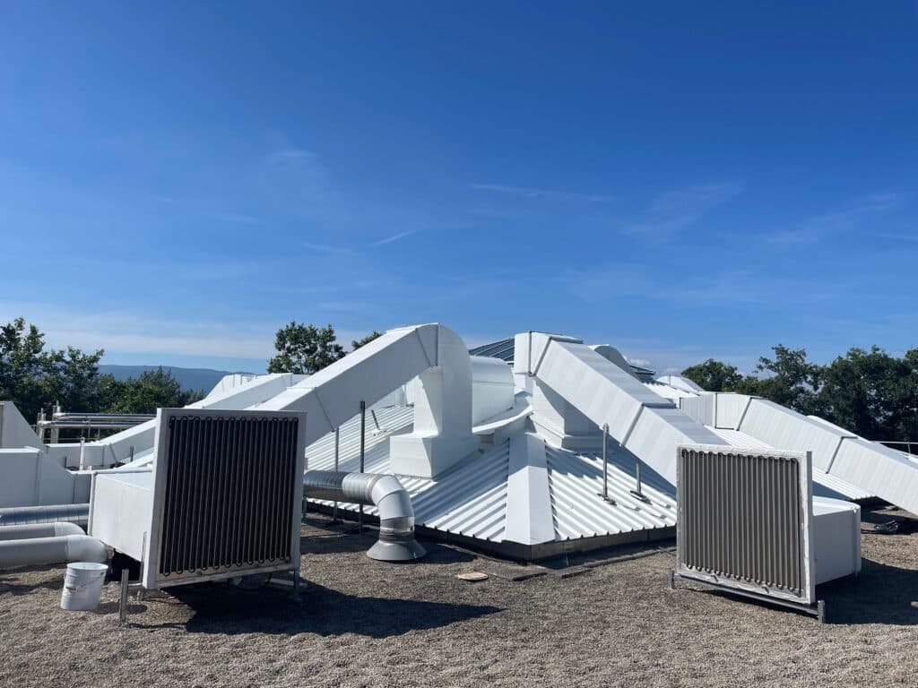 Toit d'un bâtiment avec des structures blanches et des ventilateurs sur une surface en gravier.